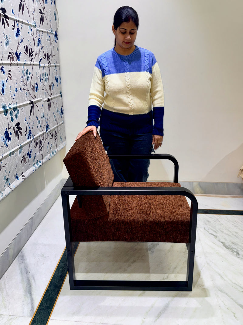 Woman standing next to a brown lounge chair in a room with floral wallpaper.