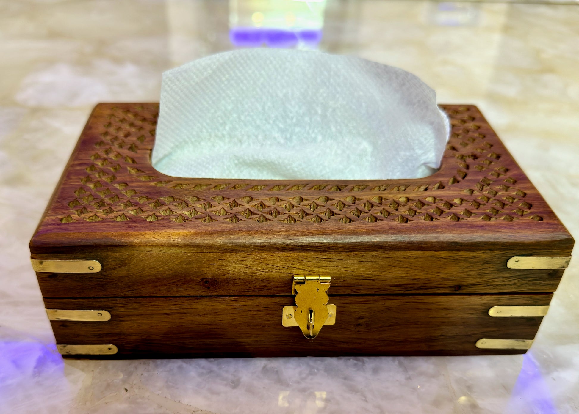 Wooden tissue box with intricate carvings and a gold latch on a marble surface.