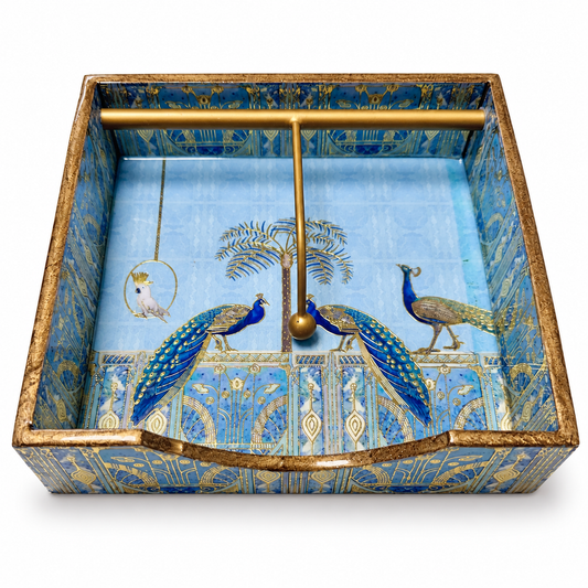 Blue decorative napkin holder with peacock artwork, gold trim and a gold retaining bar on a white background.