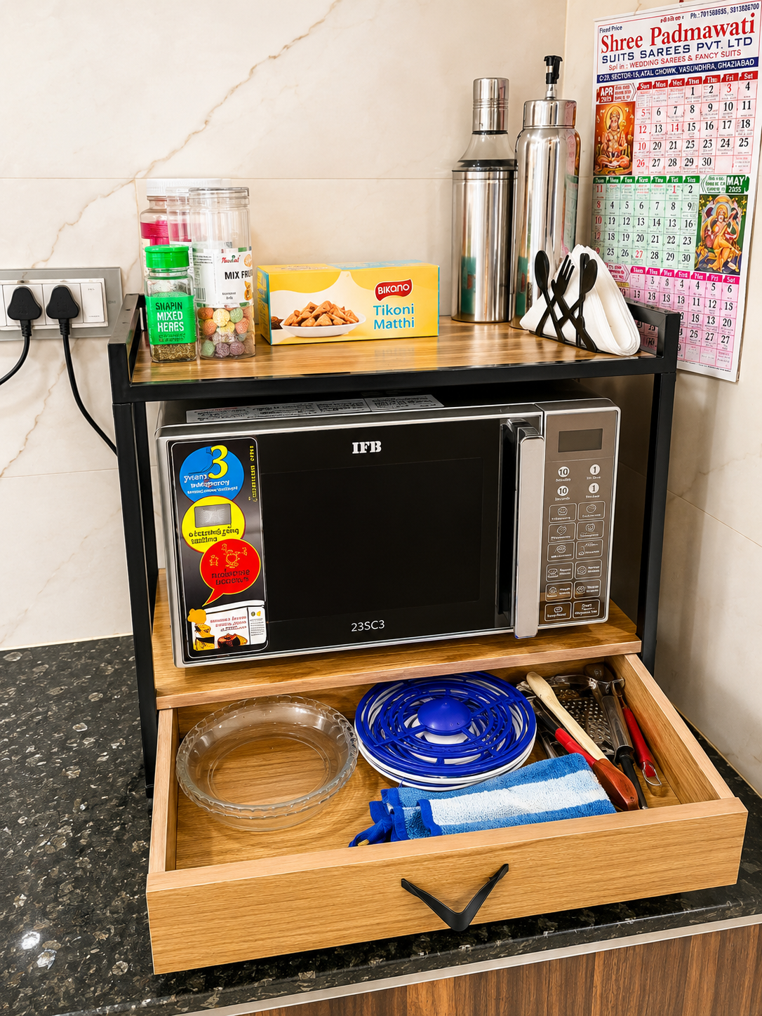 Side angle of a wooden and black metal microwave stand with pull-out drawer and organised kitchen storage setup.