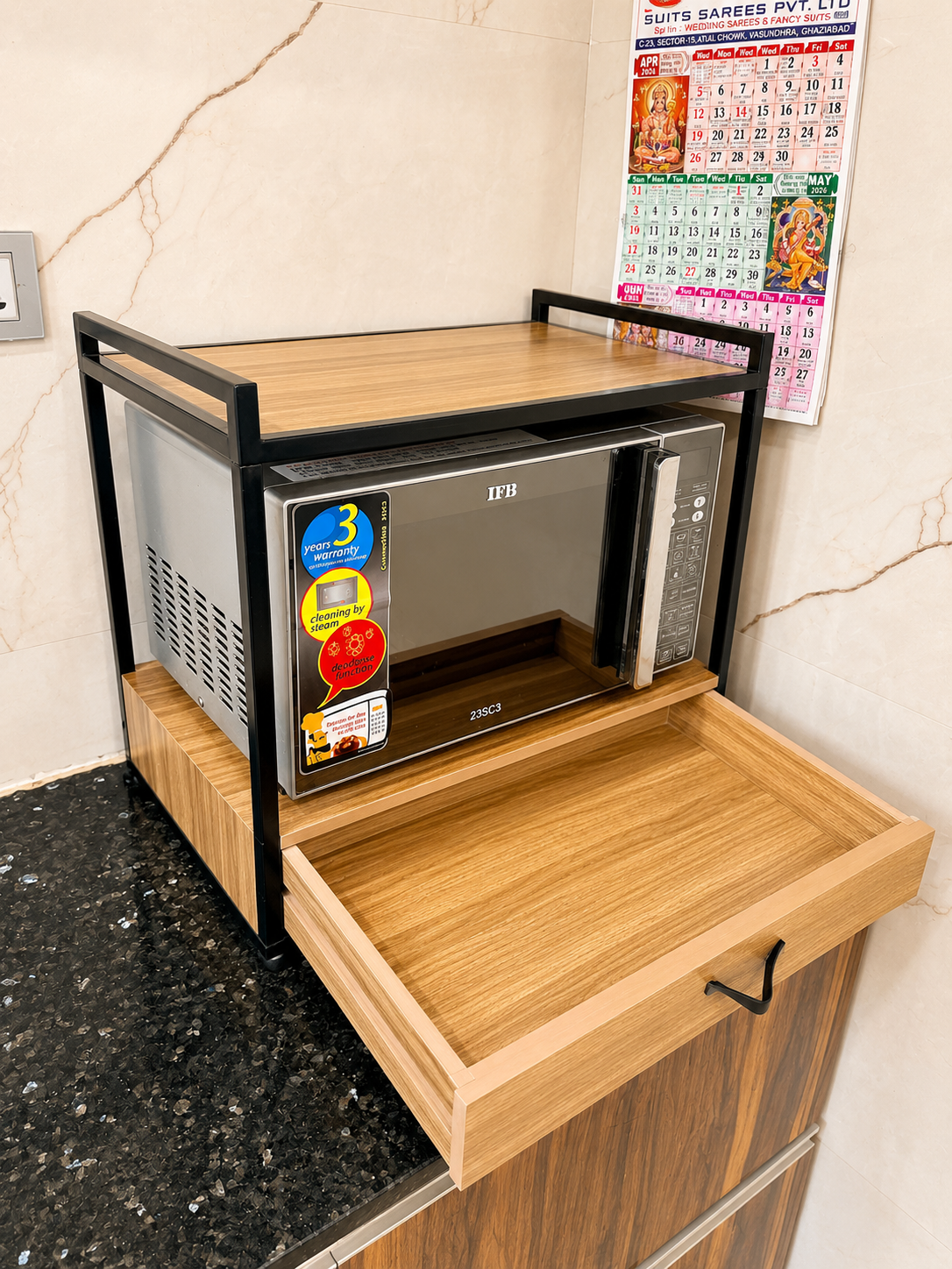 Microwave oven stand with empty pull-out drawer, wooden platform and black metal frame shown in a clean kitchen corner.
