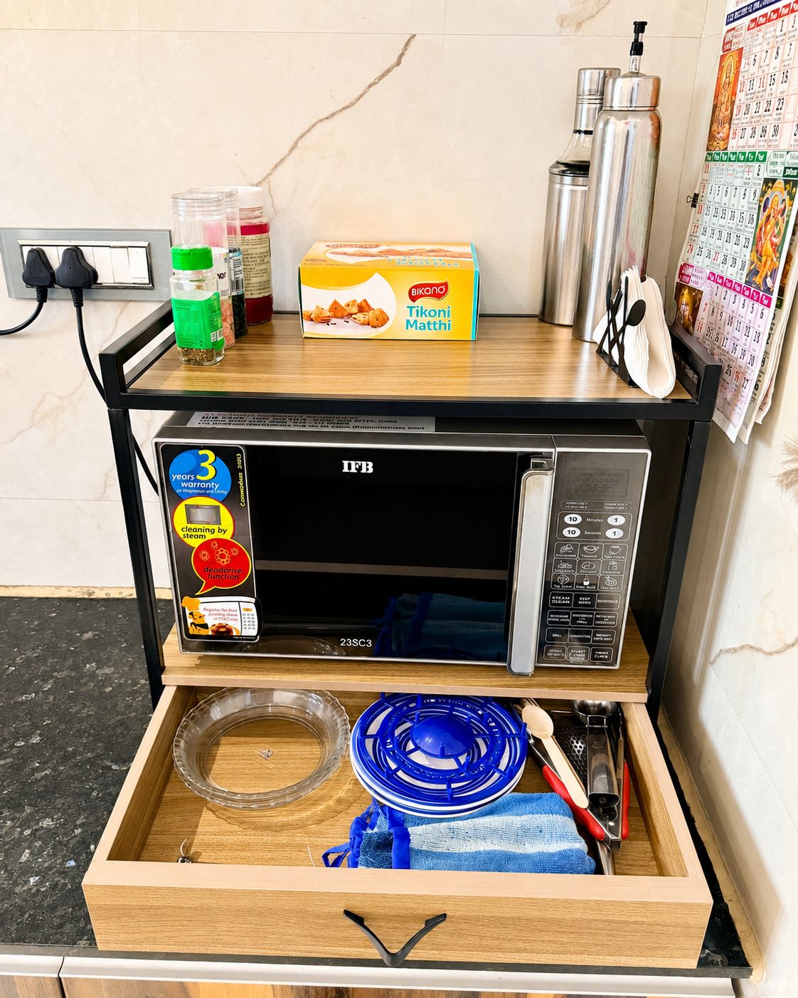 Kitchen microwave stand with open wooden drawer showing storage space for utensils, towels and kitchen accessories.