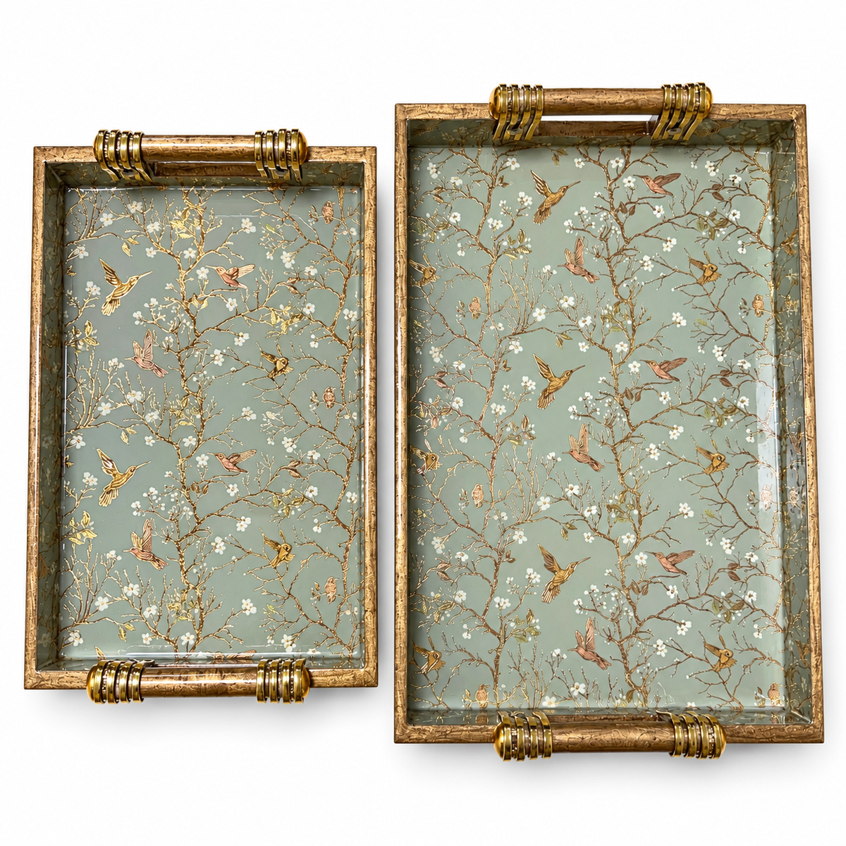 Two wooden serving trays displayed side by side, featuring sage green bird and blossom patterns and gold-accented handles on a white background.