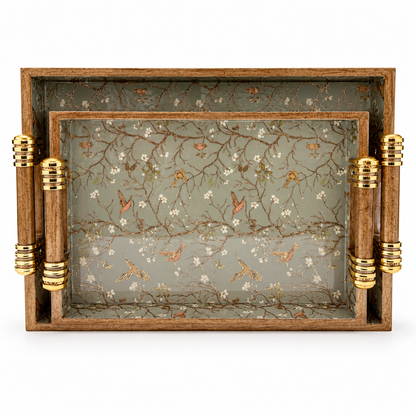 Set of two wooden serving trays with sage green bird and floral designs and gold-accented handles on a white background.
